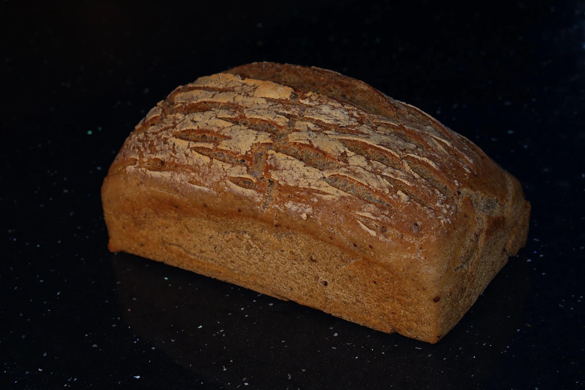 Pâine fără gluten cu crusta presărată cu făină, pe fundal negru.