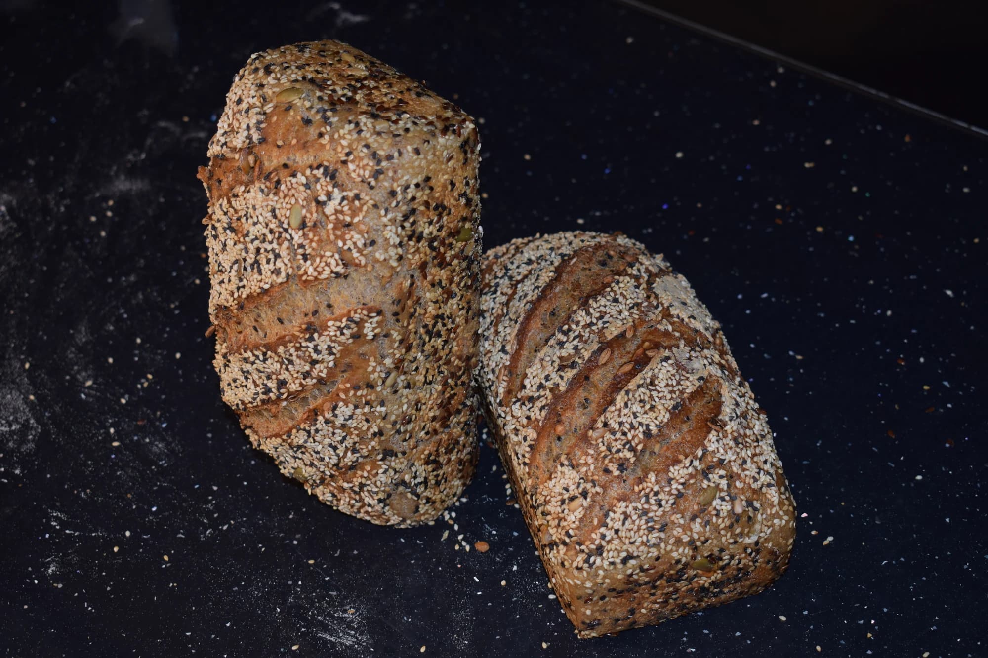 Două pâini fără gluten cu semințe, pe fundal închis.
